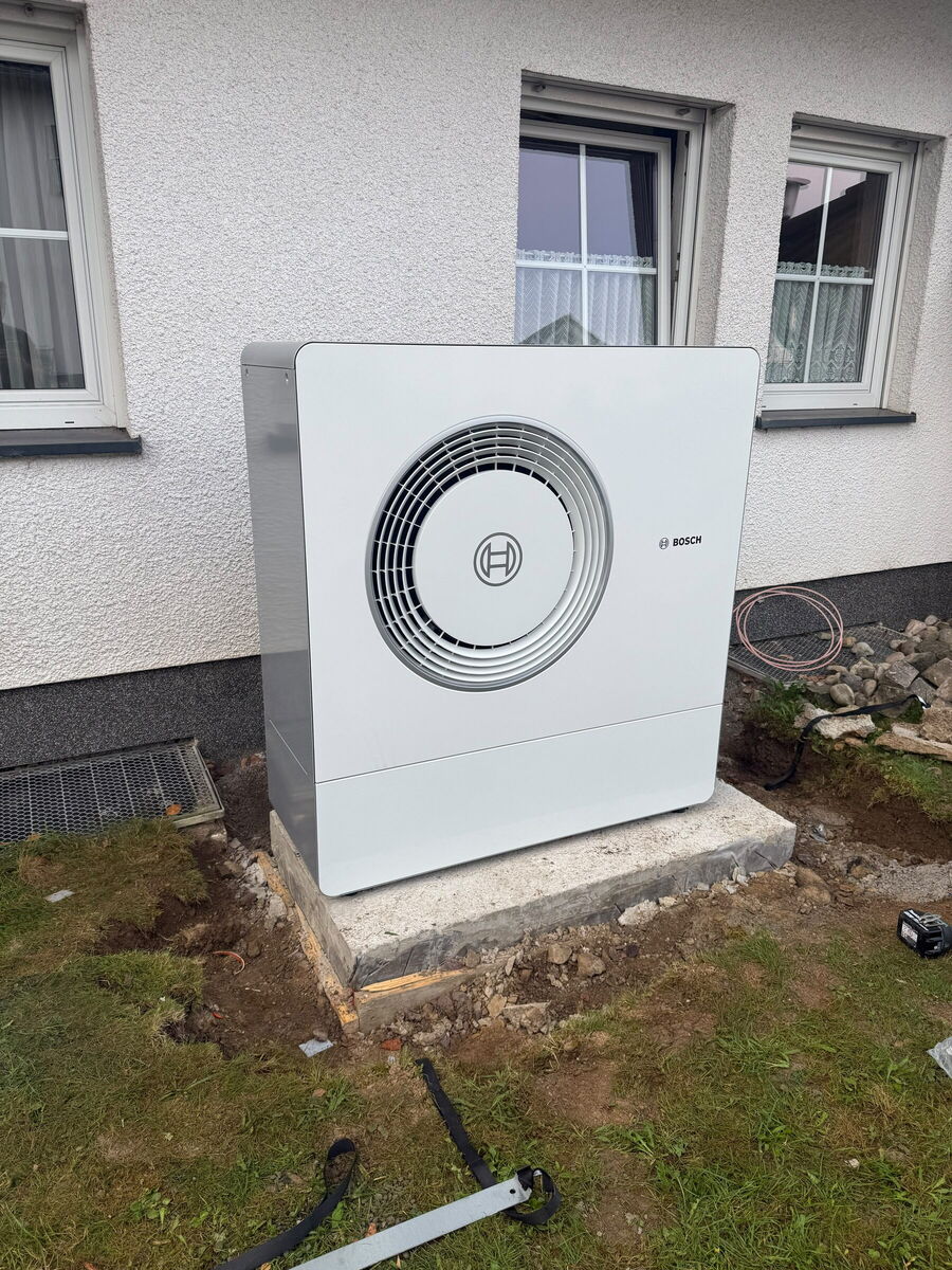 Bosch-Wärmepumpe auf frischem Fundament vor einem Wohnhaus