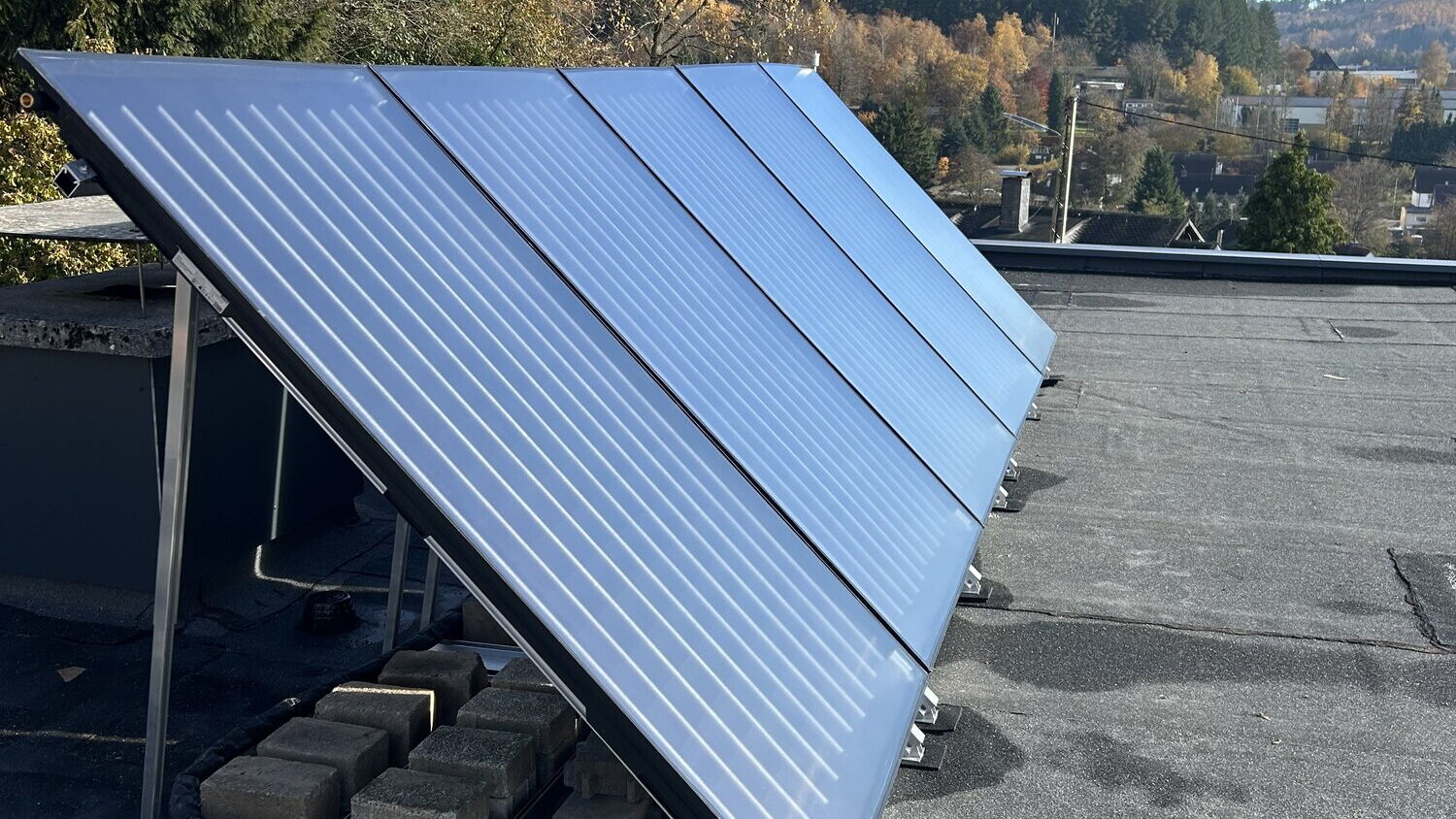 Solarthermie-Kollektoren auf einem Hausdach vor bewaldeten Hügeln