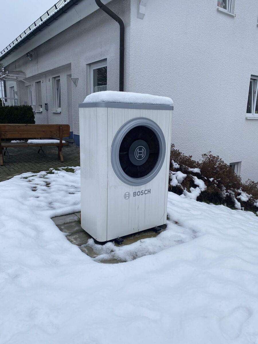 Bosch-Wärmepumpe im Schnee vor einem weiß verputzten Wohnhaus